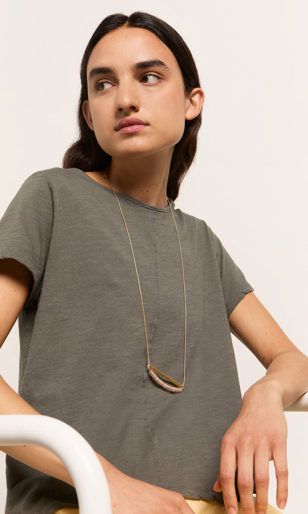 Plümo- A person with long dark hair in a gray t-shirt wears the Barillo Necklace - Clear, seated against a plain background.