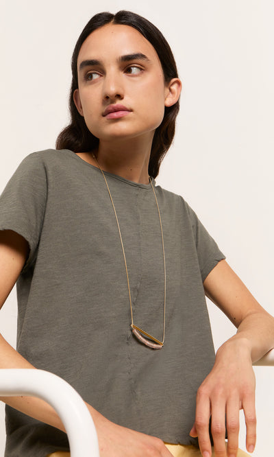 Plümo- A person with long dark hair in a gray t-shirt wears the Barillo Necklace - Clear, seated against a plain background.