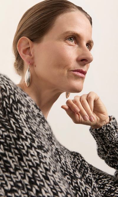 Plümo  Woman in a black and white knit sweater, chin resting on hand, wearing Bea Drop Earrings.