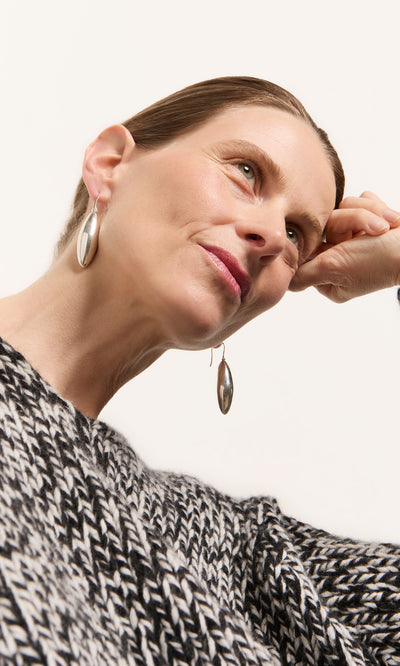 Plümo  Woman in a textured black and white sweater wears Bea Drop Earrings, looking up against a white wall.