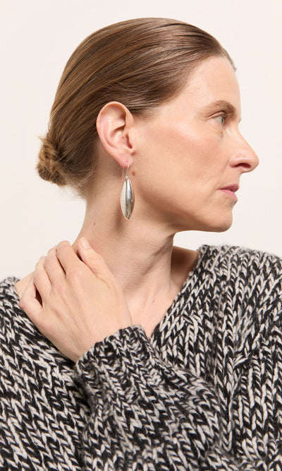 Plümo  Woman in a black and white sweater facing right, wearing Bea Drop Earrings, hair in a low bun.