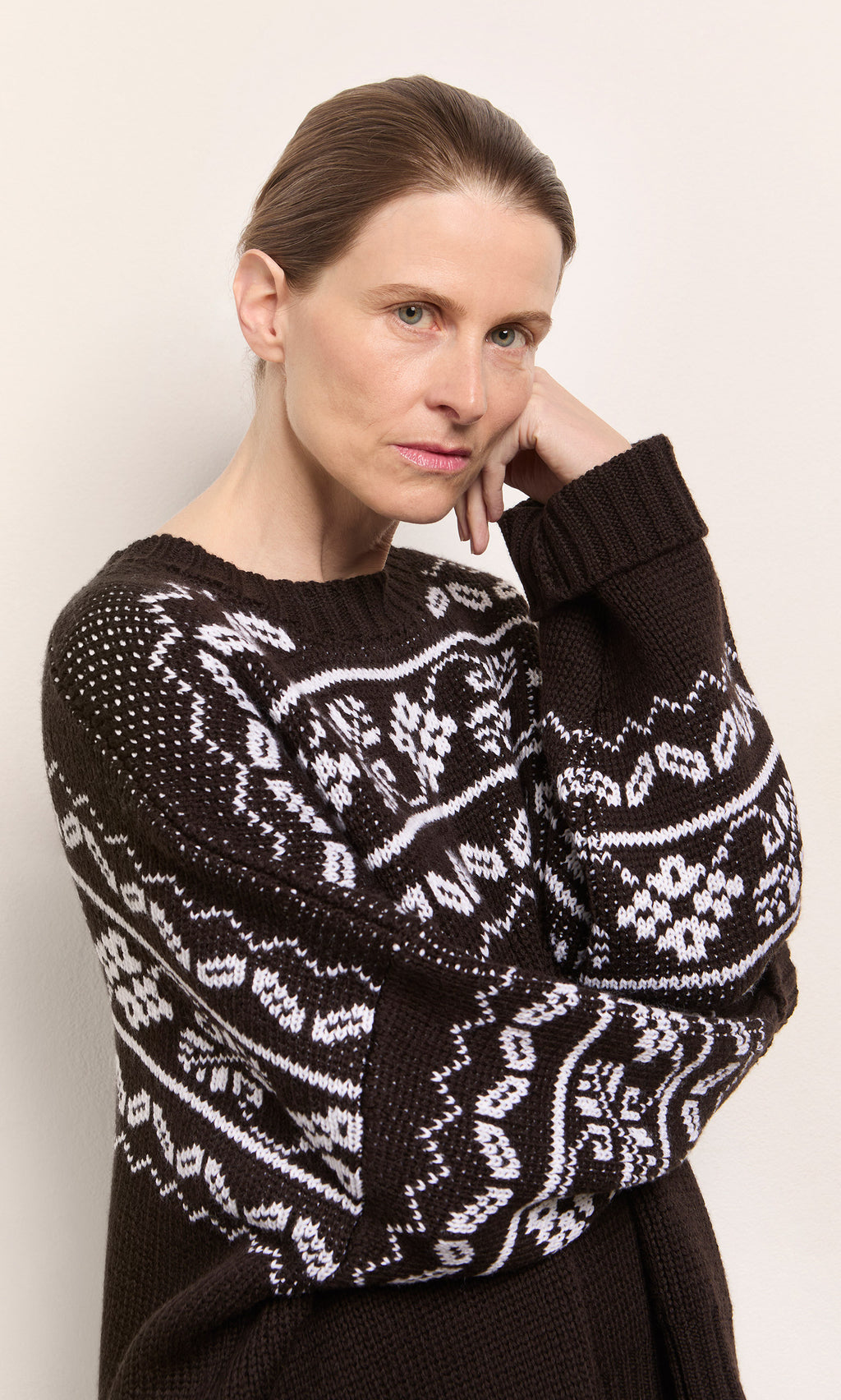 Plümo  Woman with light brown hair in the Burke Jumper, resting her head on her hand, looking serious.