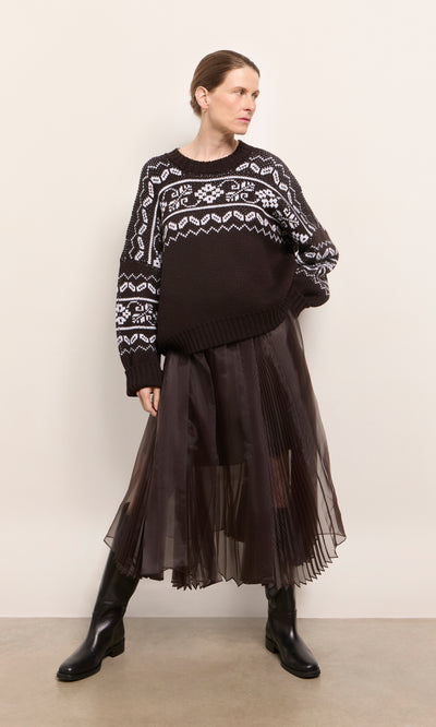 Plümo  Woman in a Kyffin Organza Skirt, black and white sweater, and black boots stands against a plain wall.