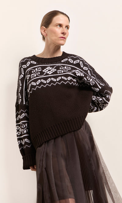 Plümo  Woman wearing the Burke Jumper and a sheer black skirt, standing against a light background.