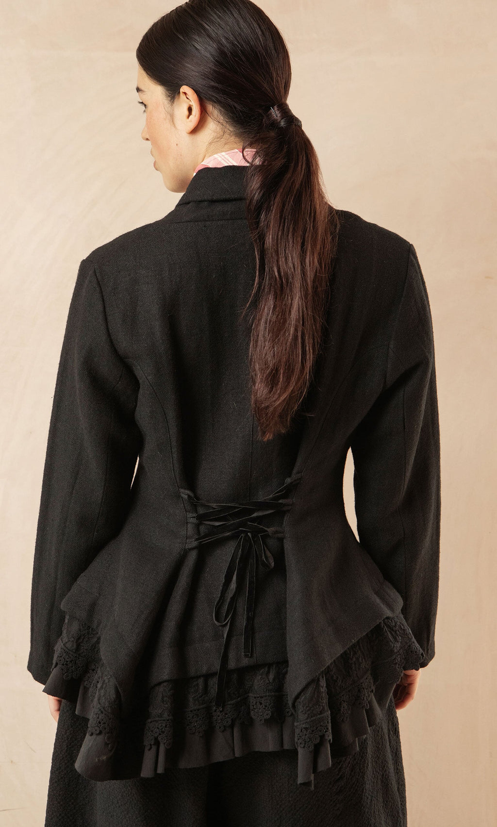 Plümo- Woman with long dark hair in a low ponytail, wearing the Cara Riding Jacket, seen from the back.