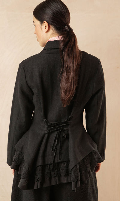 Plümo- Woman with long dark hair in a low ponytail, wearing the Cara Riding Jacket, seen from the back.