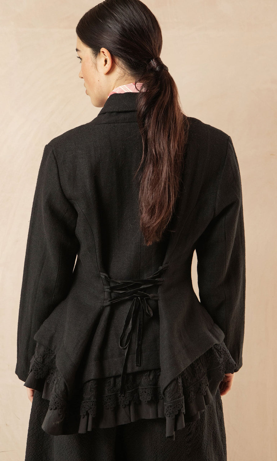 Plümo- Woman with long dark hair in a low ponytail, wearing the Cara Riding Jacket, seen from the back.