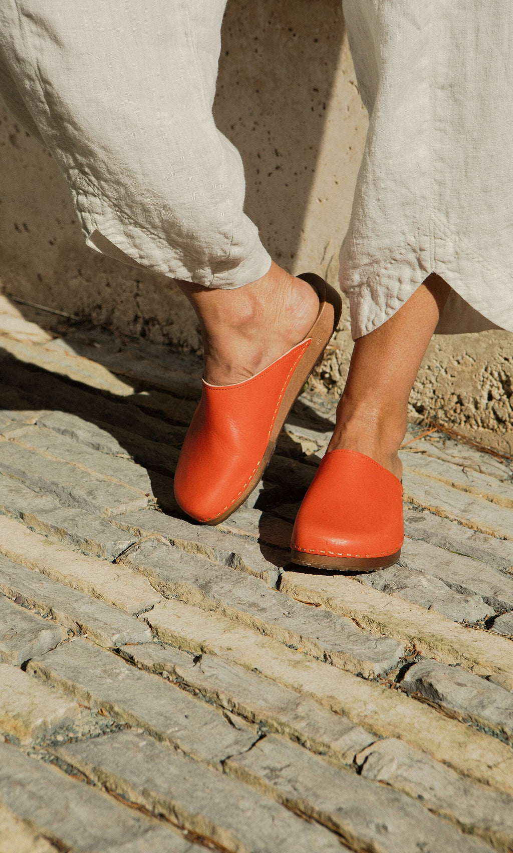 Plümo- Person wearing white pants and Carlie Clogs, designed for ergonomic comfort, on a sunlit stone pathway.