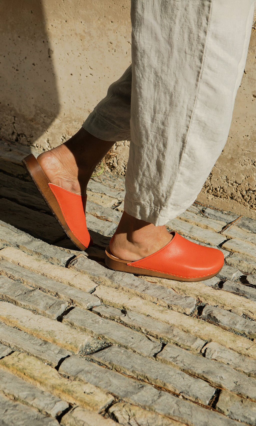 Plümo- Person in light pants and Carlie Clogs - Photoshoot Sample walking on a sunlit stone path.