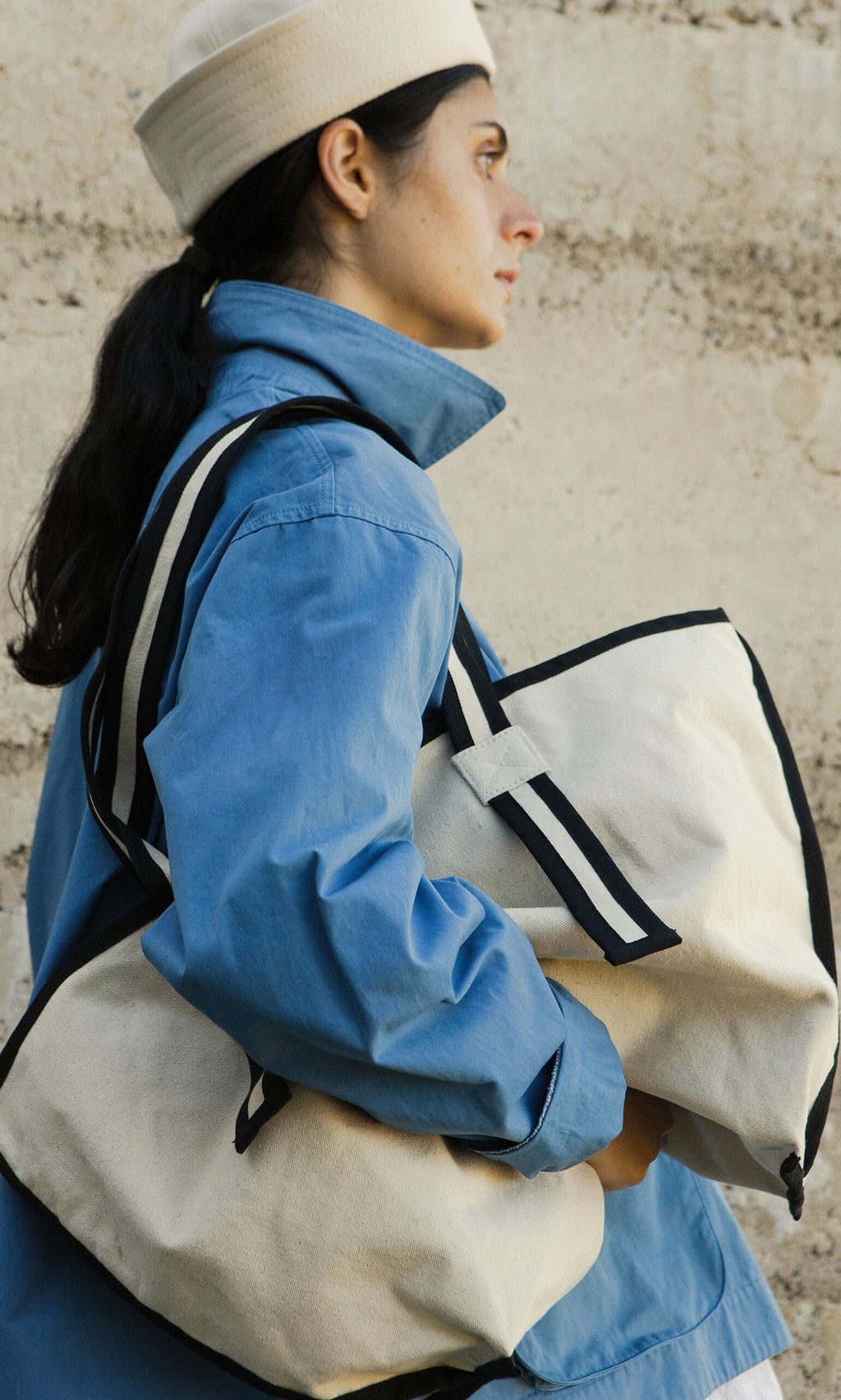Plümo- Woman in a light blue jacket and cream hat holding two Carryall Bags, standing outside.