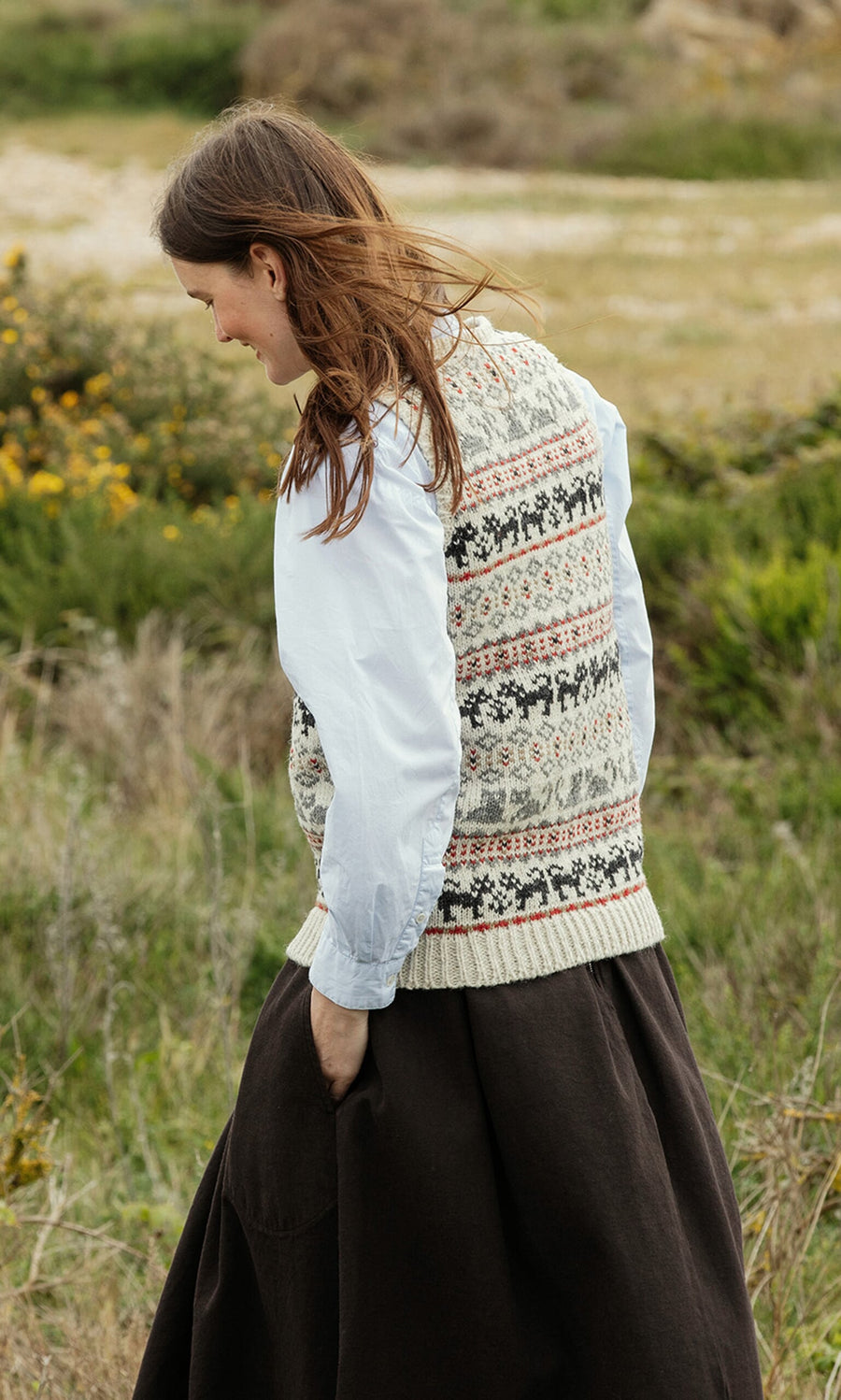 Plümo- A woman in a Cat Tank Top, handknitted in Nepal, walks outdoors wearing a white blouse and brown skirt.