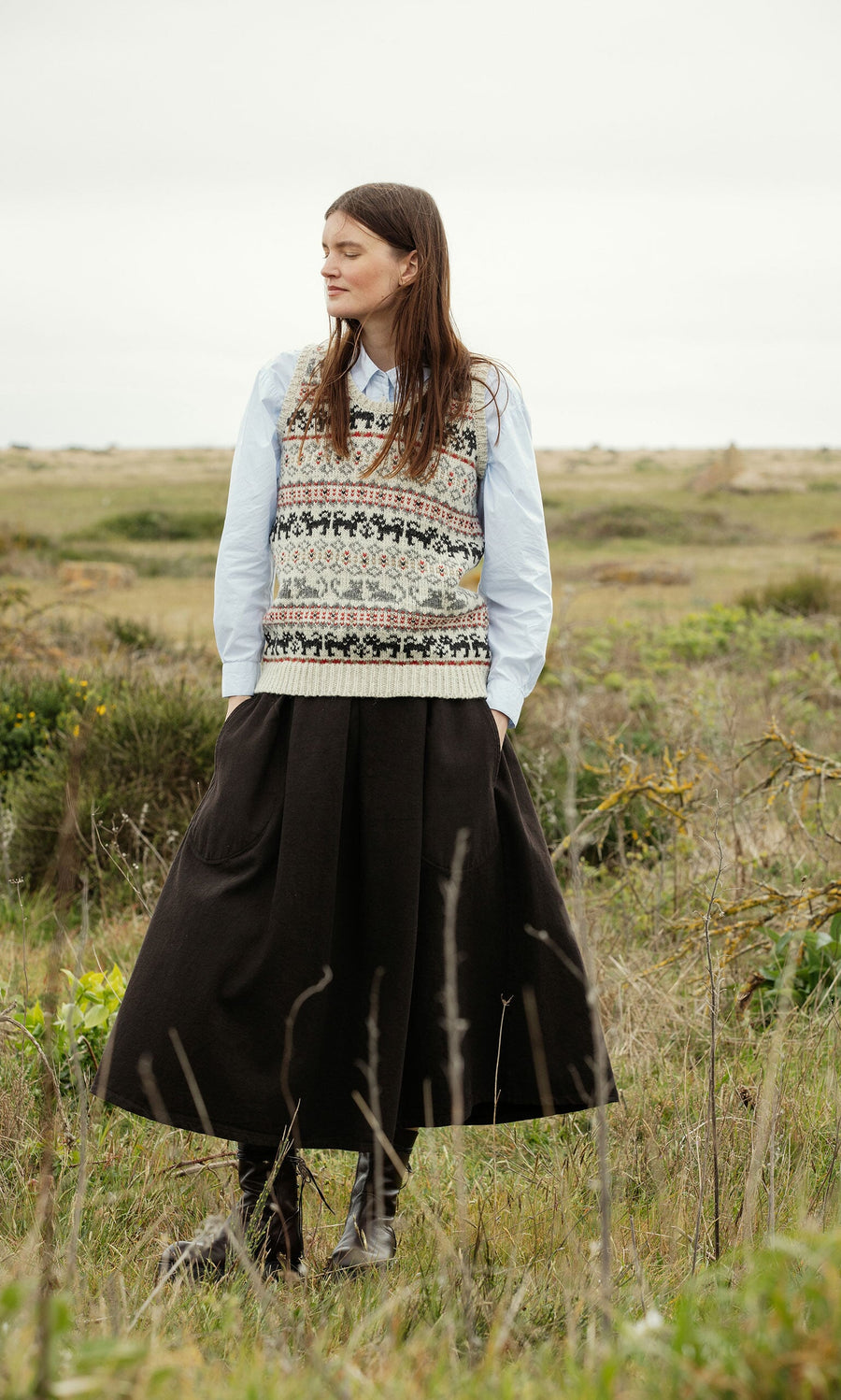 Plümo- Woman in a grassy field wears a Cat Tank Top, blue shirt, and long black skirt.