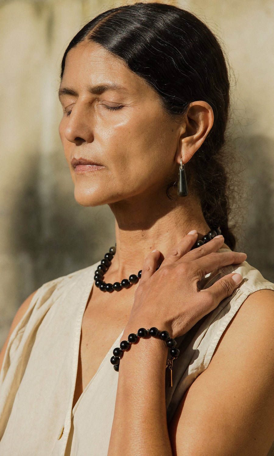 Plümo- Woman with closed eyes wears Hera Earrings, resting her hand on her chest while standing in sunlight.