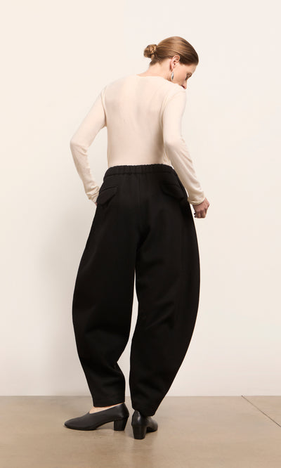 Plümo  Person facing away in beige top and Circle Pants - Boiled Black, elasticated waist, made in London, on light floor.