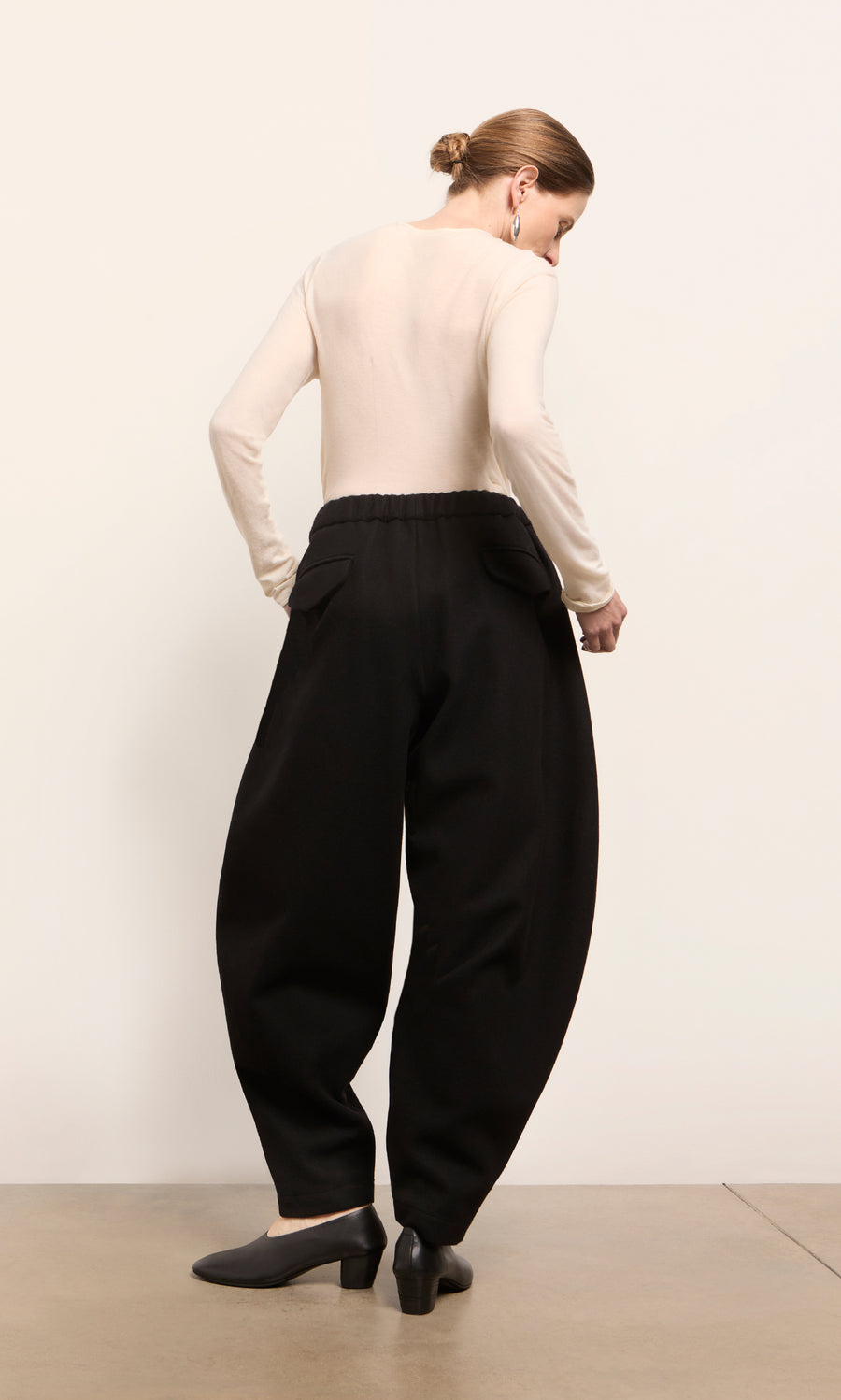 Plümo  Person facing away in beige top and Circle Pants - Boiled Black, elasticated waist, made in London, on light floor.