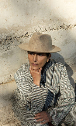 Plümo  A person in a striped jacket and the Noma Felted Hat sits outdoors, chin on hand, looking thoughtful.