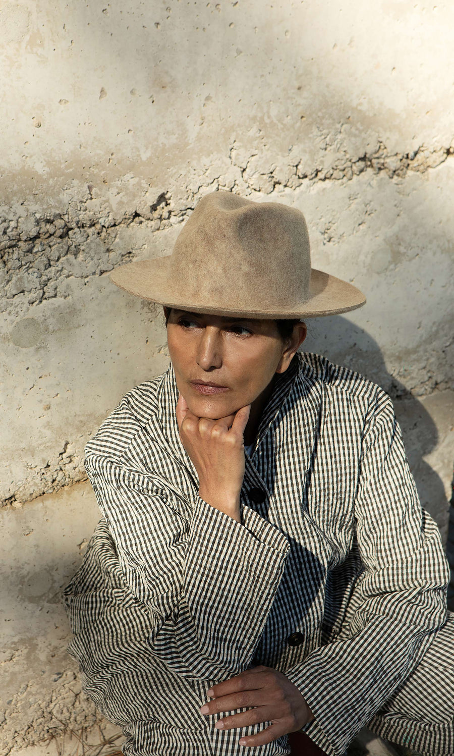 Plümo  A person in a striped jacket and the Noma Felted Hat sits outdoors, chin on hand, looking thoughtful.