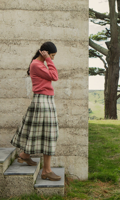 Plümo- Woman in pink sweater and Hawksmoor Kilt stands on outdoor steps in Dublin beside a concrete wall.