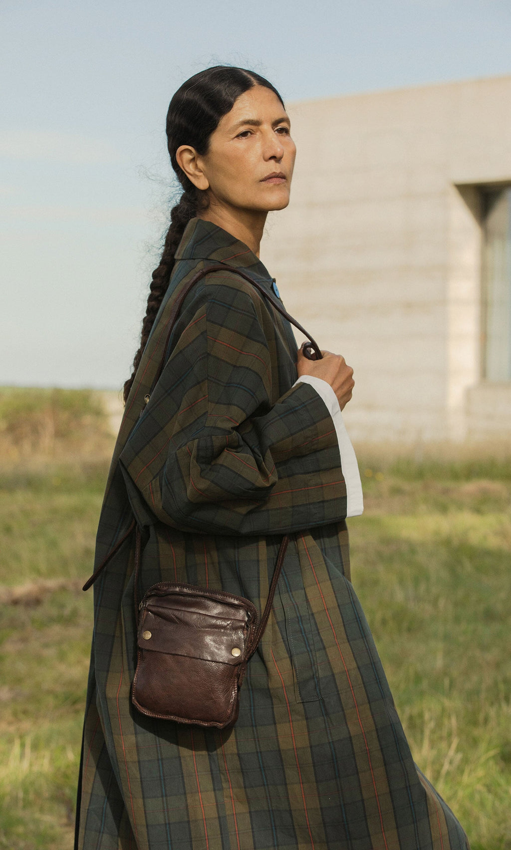 Plümo- Woman with long dark braid in plaid coat stands outdoors, carrying the Orton Parcel Bag.