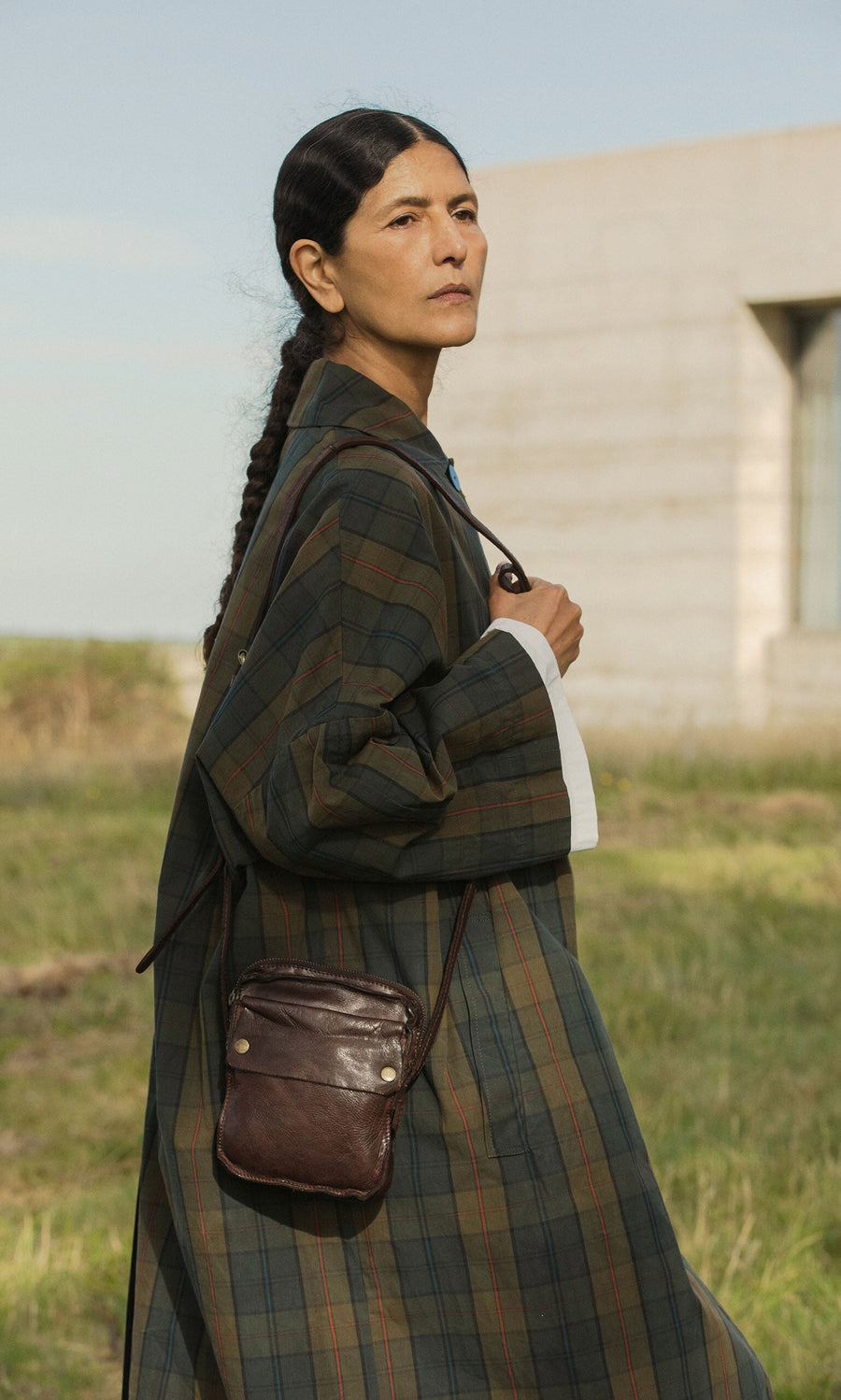 Plümo- Woman with long dark braid in plaid coat stands outdoors, carrying the Orton Parcel Bag.