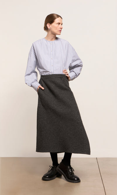 Plümo  Woman in a striped shirt and Eardley Skirt stands indoors, looking to the side with hands in pockets.