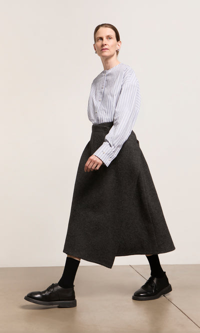 Plümo  Person in a striped blouse, Eardley Skirt, black socks, and shoes walks indoors on a light-colored floor.
