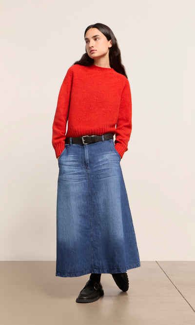 Plümo  Person in a red sweater, Eday Denim Skirt, black belt, and shoes stands against a plain background.