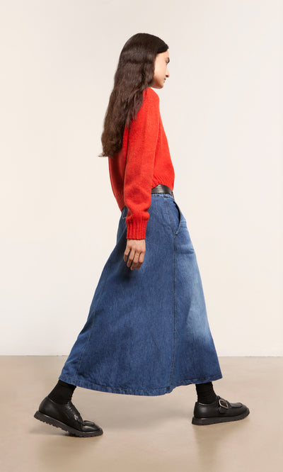 Plümo  Woman in red sweater and Eday Denim Skirt, high waist indigo, side profile, black shoes/socks—made in Italy.