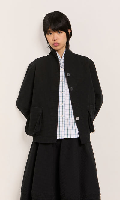 Plümo  Individual in the Envoy Jacket - Coal over a checkered shirt, set against a plain light background.