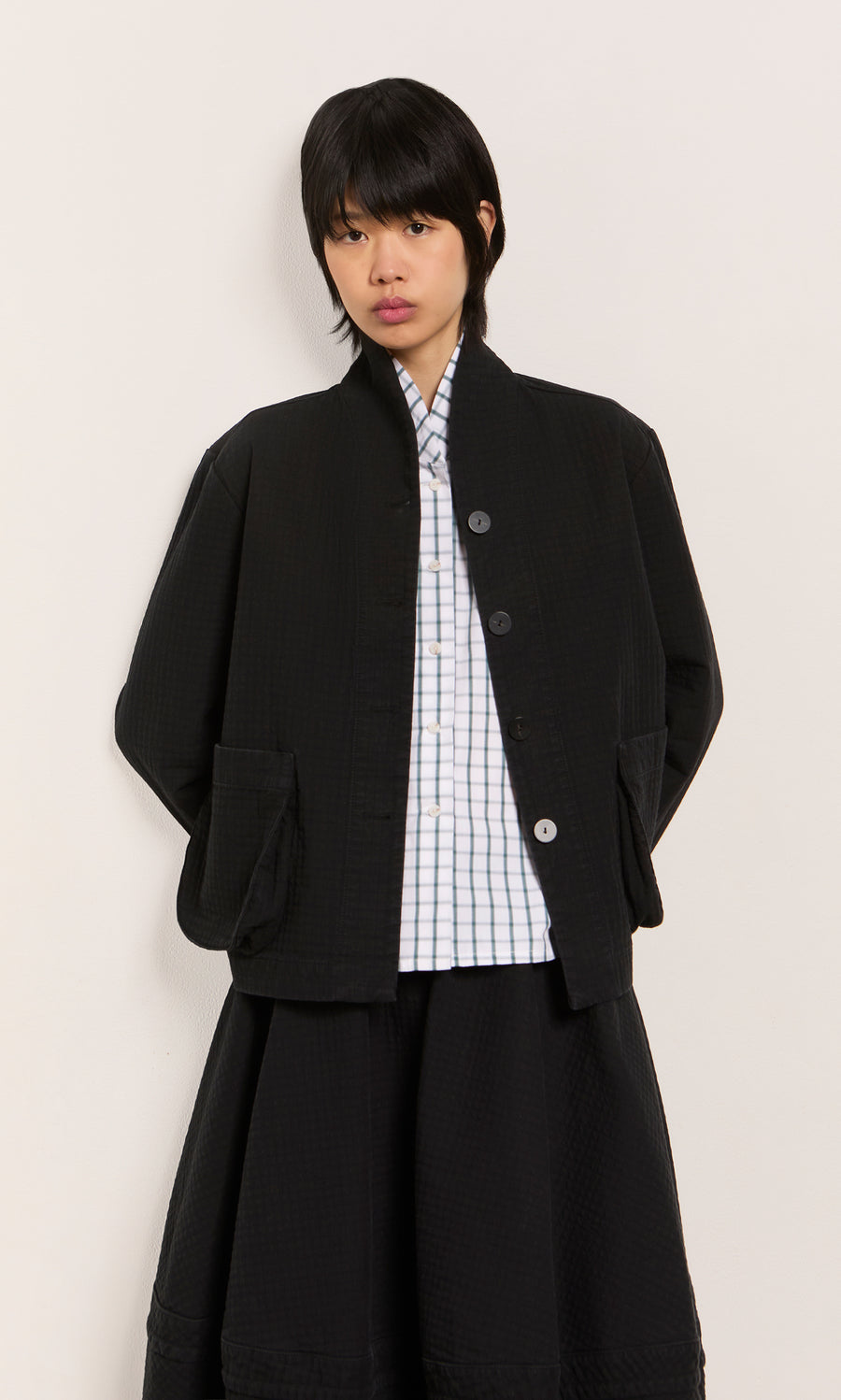 Plümo  Individual in the Envoy Jacket - Coal over a checkered shirt, set against a plain light background.