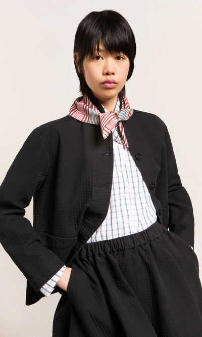Plümo  A person with dark hair in an Envoy Jacket - Coal, a green-white plaid shirt, and a red-white striped scarf.