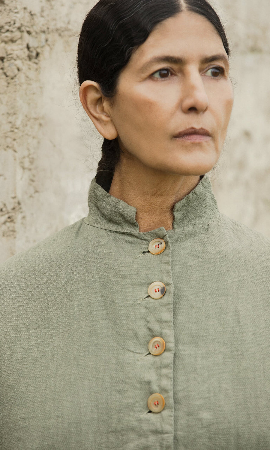 Plümo- A woman with dark hair in a braid wears the Frances Jacket by Hannoh Wessel, standing by a textured wall.