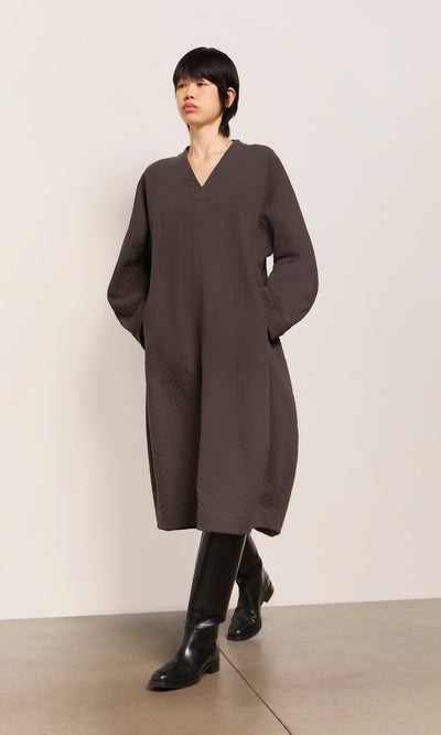 Plümo  Person in a loose, textured Grenyer Dress with long sleeves and tall black boots walking indoors.
