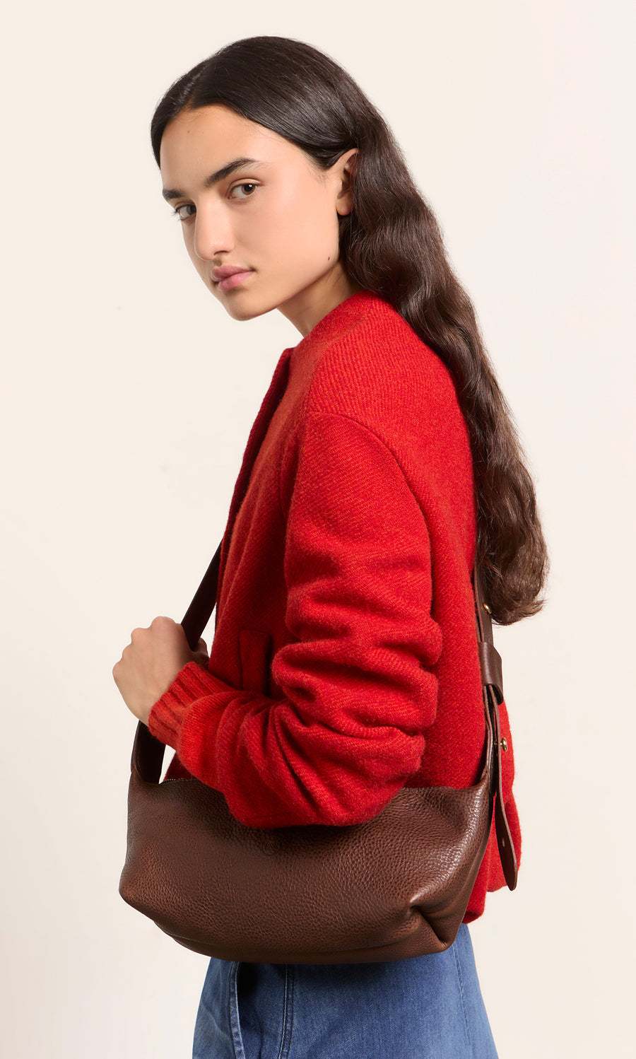 Plümo  Woman in a red sweater with long brown hair holds the Hattie Bag, looking at the camera.