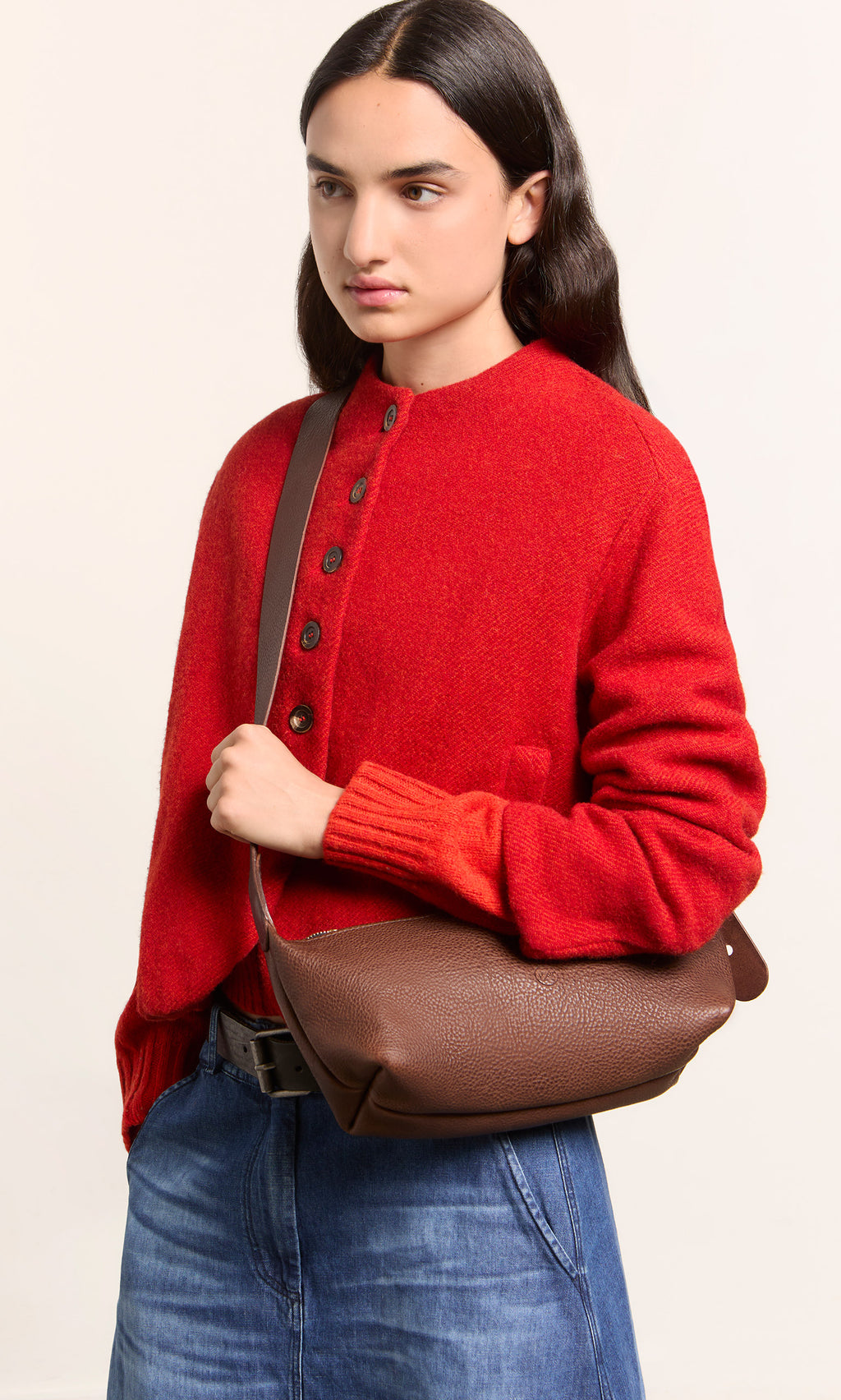 Plümo  Person in red sweater, blue jeans, with the Hattie Bag, on a plain background.