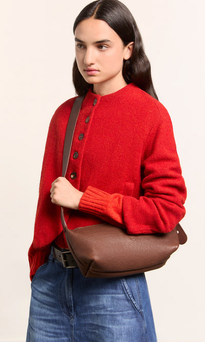 Plümo  Person in red sweater, blue jeans, with the Hattie Bag, on a plain background.