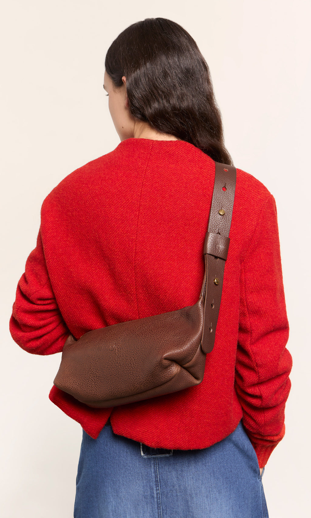 Plümo  Woman in red jacket with a designer Hattie Bag crossbody sling and blue jeans, seen from behind.