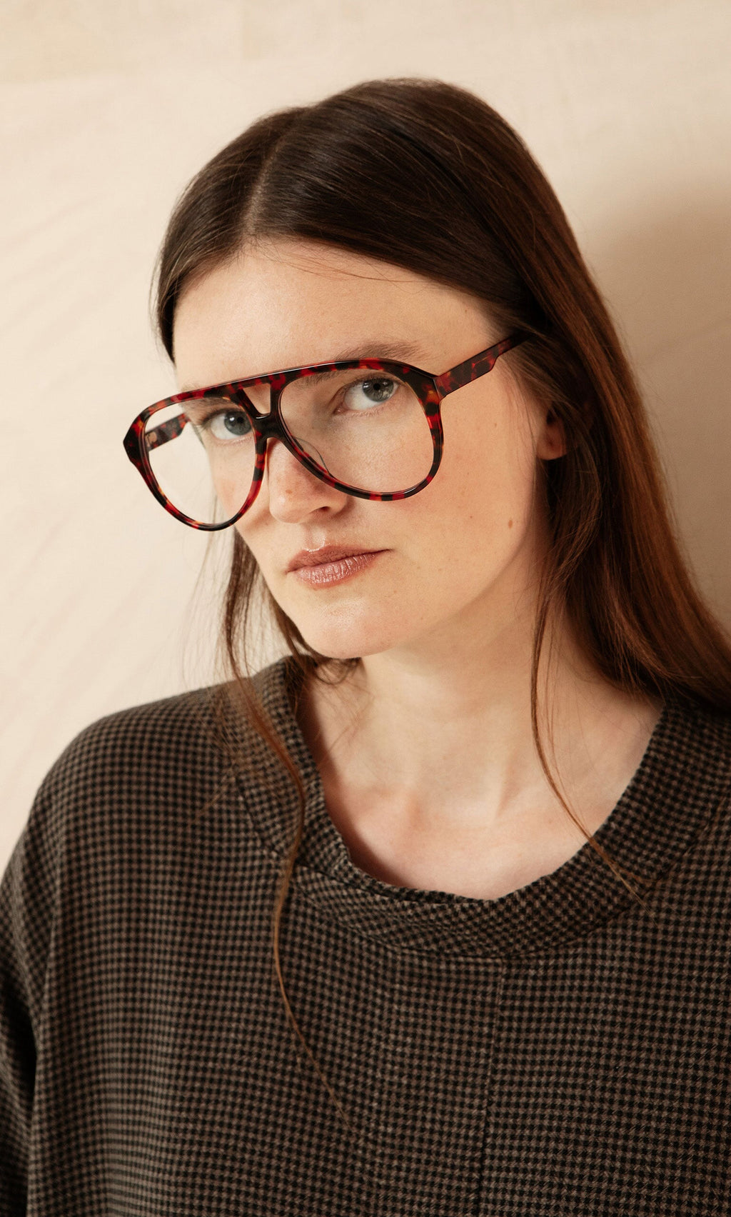 Plümo- Woman with long brown hair wears Havana Red Readers and a dark textured top, looking at the camera.