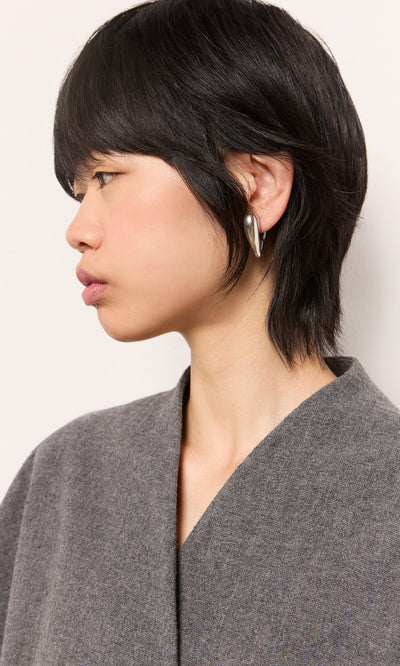 Plümo  Person with short black hair wears a gray top and Silver Heart Earrings, facing left against a light background.