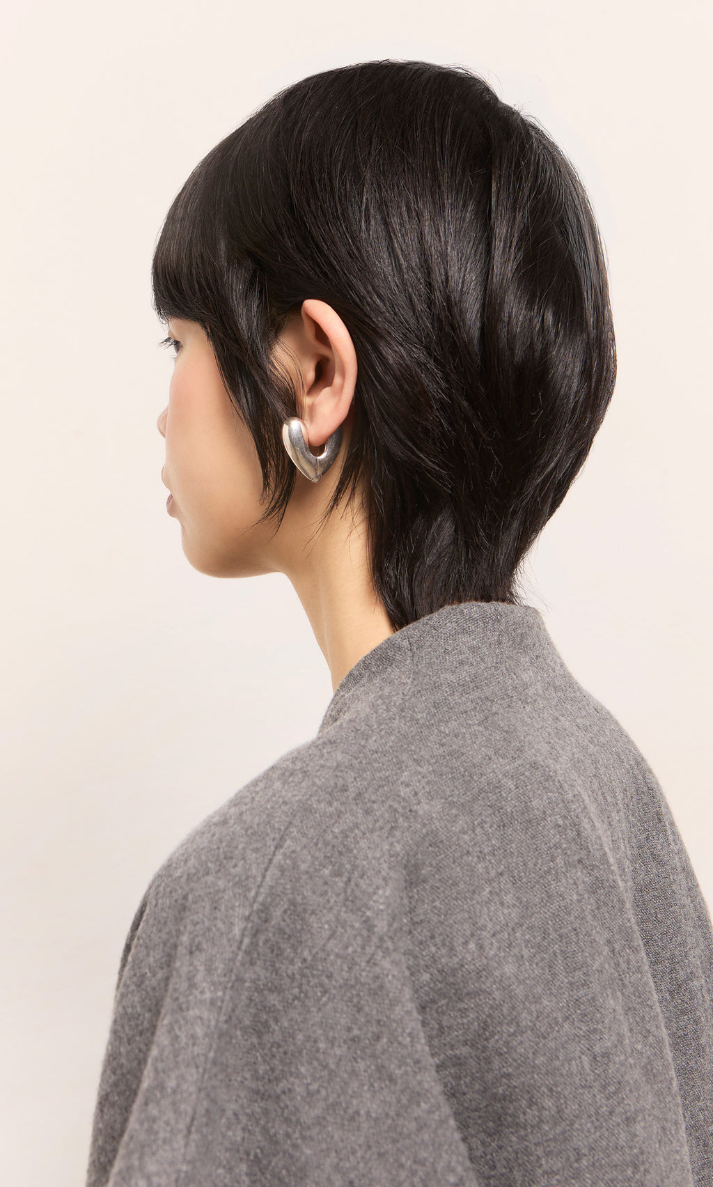 Plümo  Person with short black hair in a gray top, wearing Silver Heart Earrings, facing away.