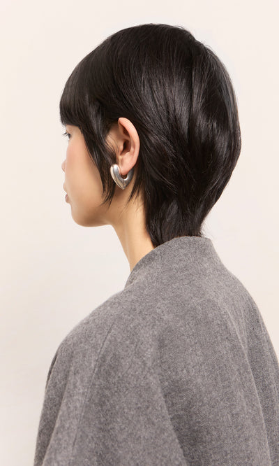 Plümo  Person with short black hair in a gray top, wearing Silver Heart Earrings, facing away.