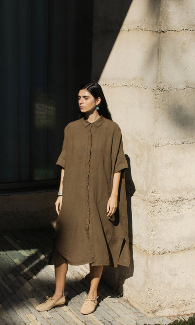Plümo- Woman in the Hockley Linen Dress with raw edge collar stands in sunlight against a concrete wall, looking to the side.