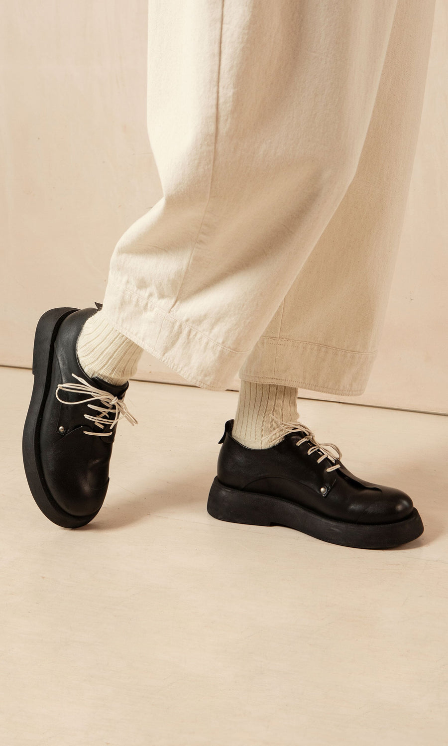 Plümo- Person wearing cream wide-leg pants, cream socks, and Hosier Brogues walking indoors on a light floor.