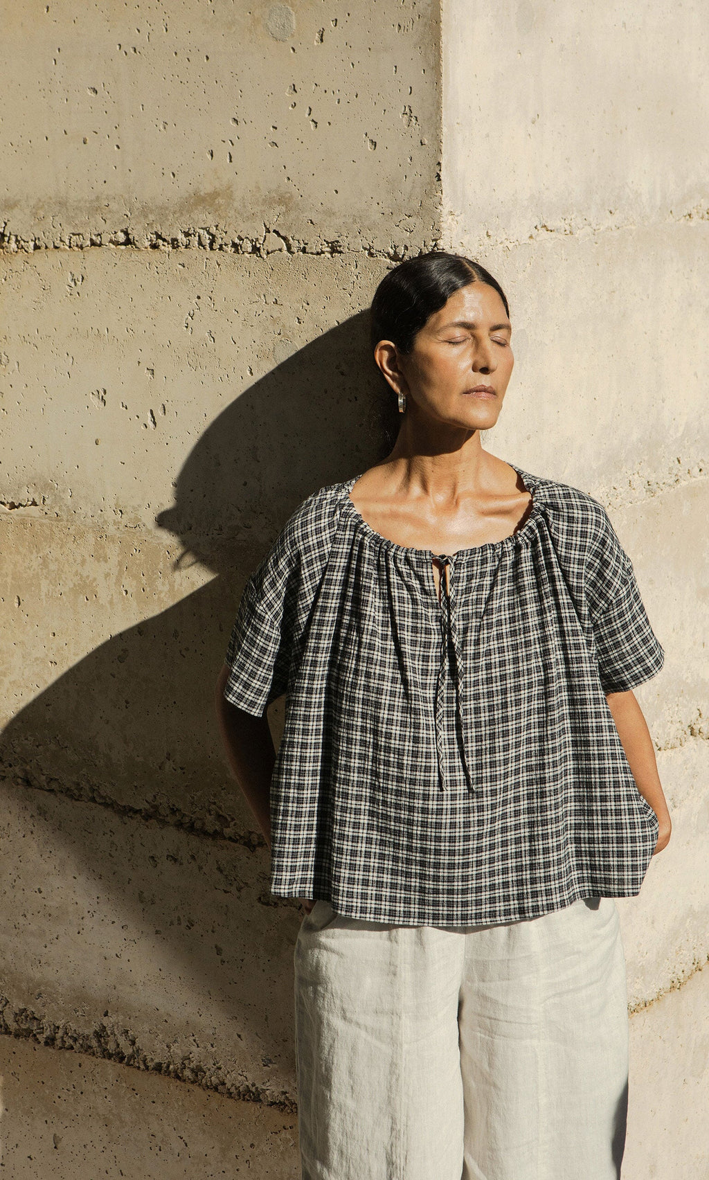 Plümo- Woman in a plaid top and white pants basks in sunlight, wearing handmade Hui Hoops silver earrings.