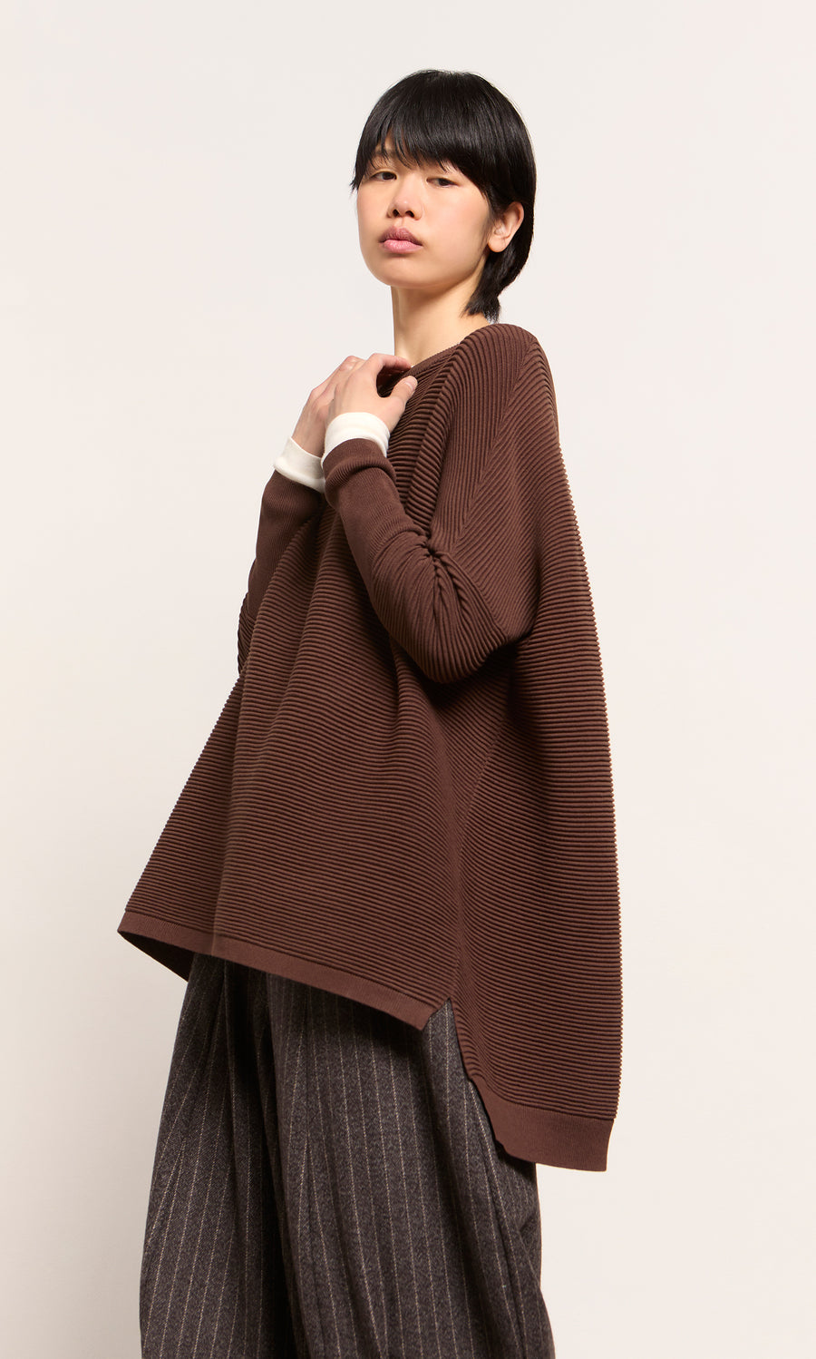 Plümo  Person in a Jack Sweater - Bitter Chocolate by Plümo Studio and wide pinstripe pants stands against a plain light background.