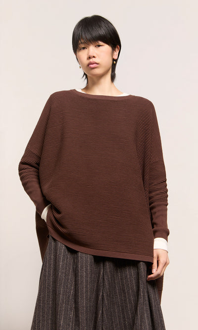 Plümo  Model wears Jack Sweater - Bitter Chocolate in plant-based yarn, styled by Plümo Studio with a pinstriped skirt.