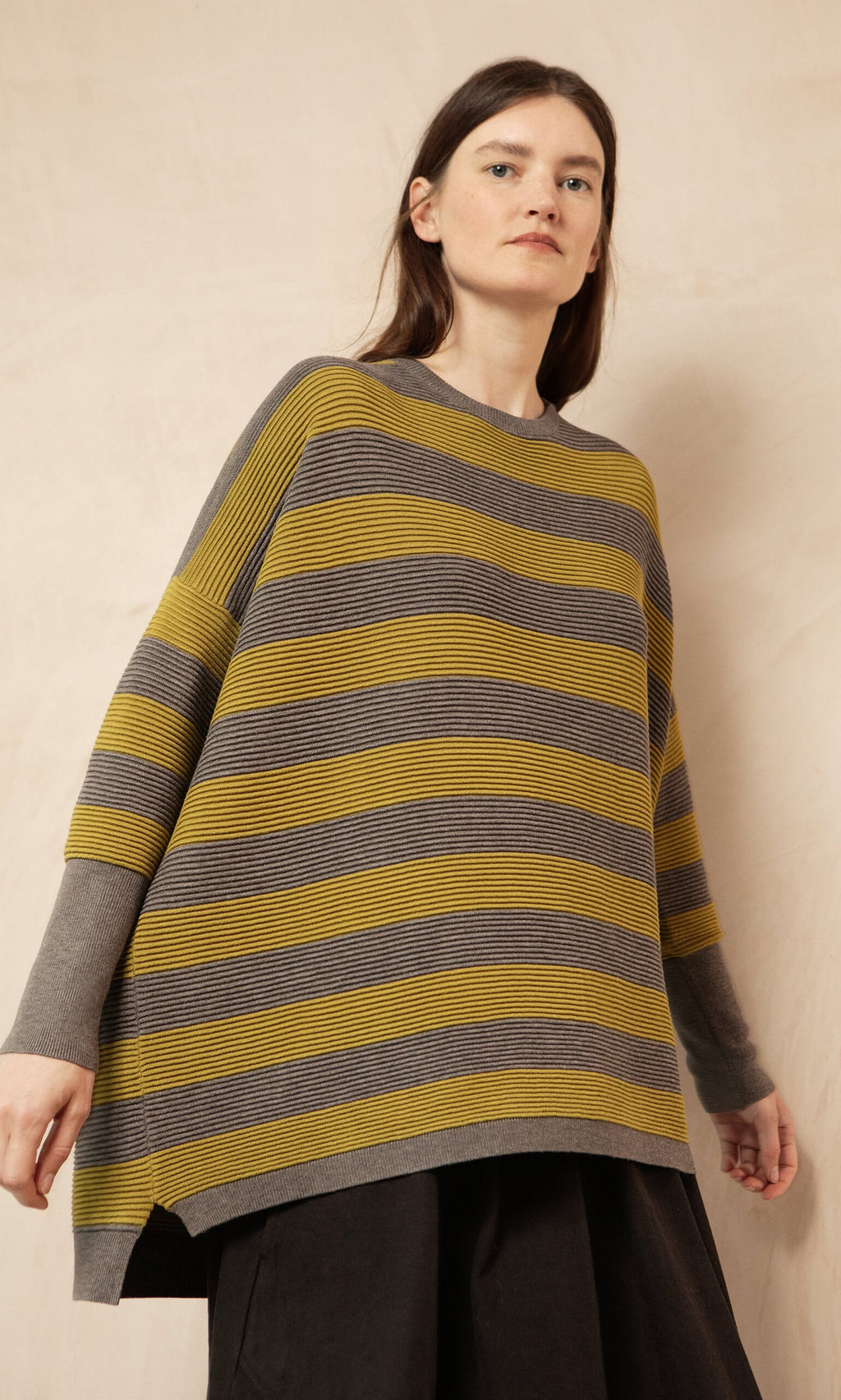Plümo- Woman wears Plümo Studio's Jack Sweater - Butter Stripe with yellow and gray stripes, wide sleeves, and dark pants.