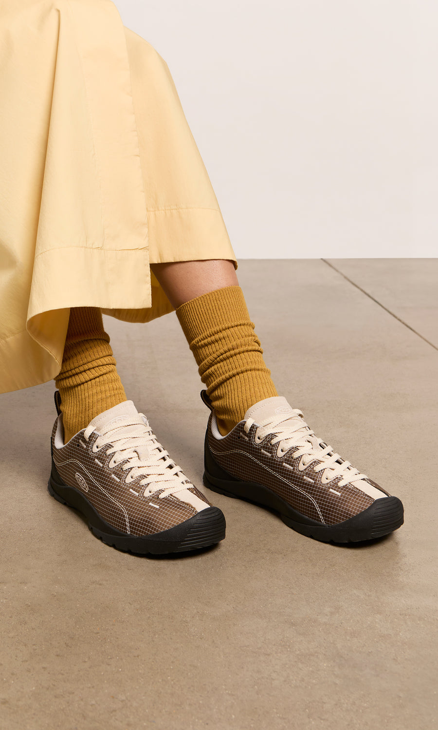 Plümo  Person wears Walking Shoes, mustard socks, beige pants, seated on a smooth, light-hued floor.