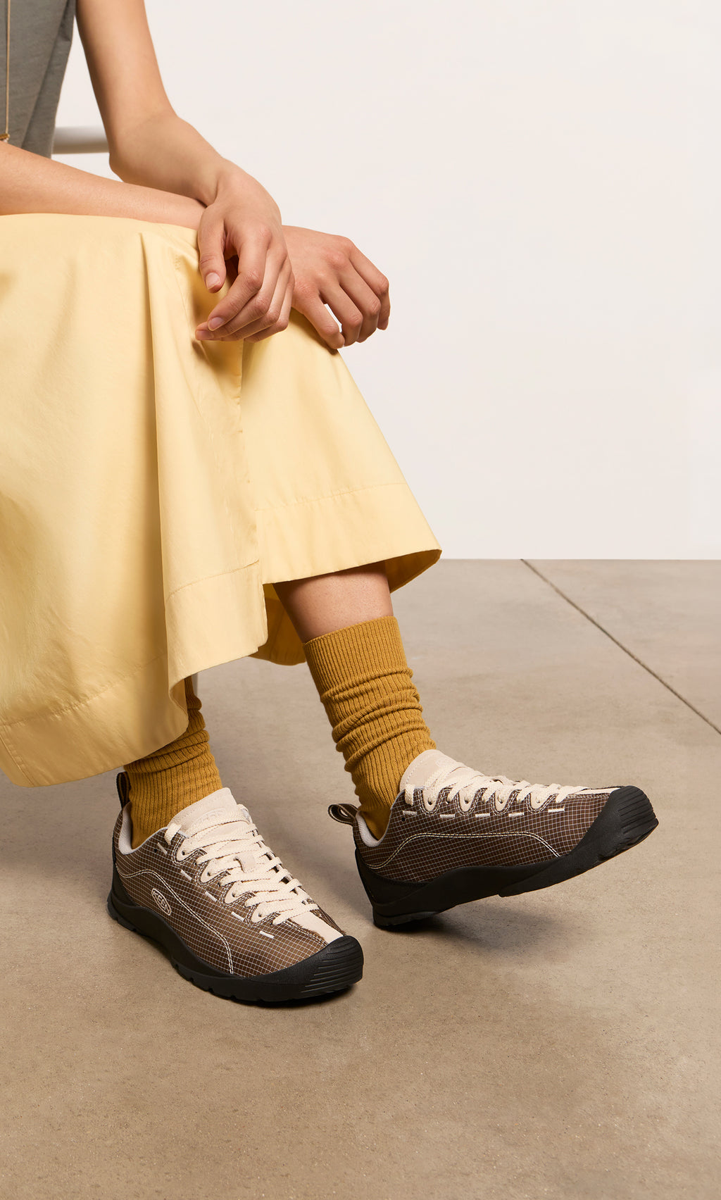 Plümo  Person in a yellow skirt wearing Walking Shoes with breathable canvas, sitting on a concrete floor.