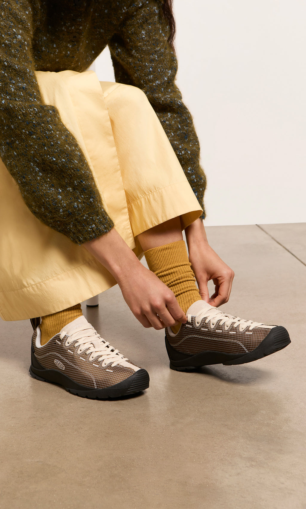 Plümo  Person tying beige Walking Shoes, wearing yellow socks and skirt, sitting on a bench.